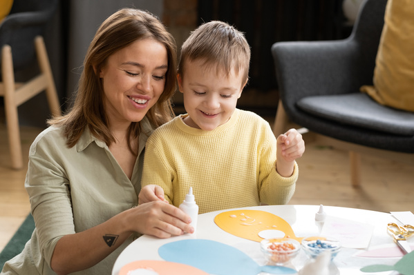 A mother in a light shirt helps her son in a yellow sweater to make an Easter card with an applique