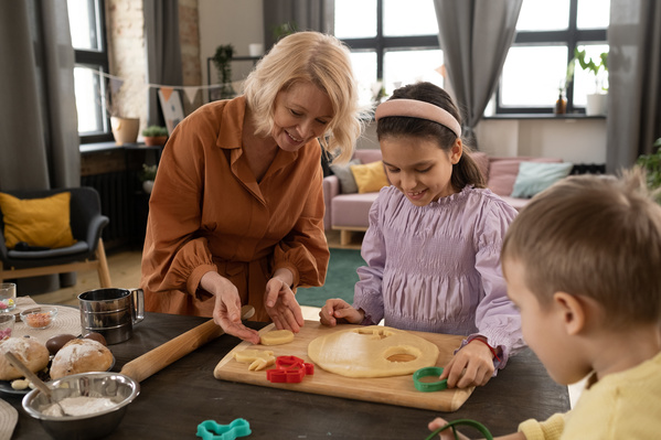 Granny with blonde hair helping her granddaughter in a pink blouse to make Easter cookies