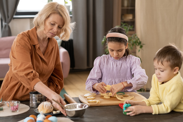 Granny with blonde hair making Easter gingerbread with her granddaughter in a pink blouse and grandson in a yellow sweater