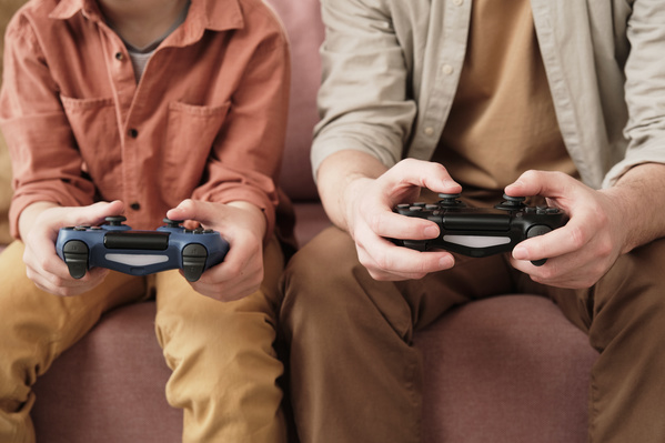 Game controllers of dark shades in the hands of a father and son playing a video game sitting on the couch
