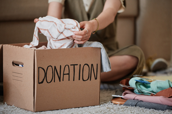 A striped piece of clothing is placed in a cardboard donation box on a light carpet