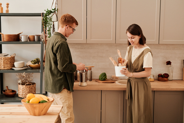 A couple of young people in a bright kitchen holding eco-friendly wooden kitchen accessories