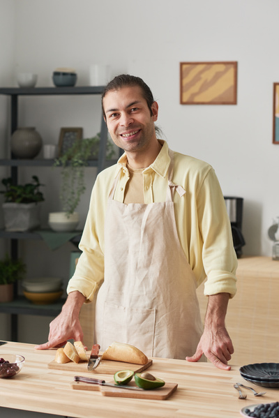 A smiling man in a light apron is behind the table with the products on it in a light kitchen