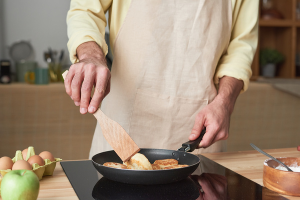 Sweet cheese fritters in a frying pan are turned over by a man in a light apron with a cooking spatula