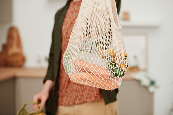 A white cotton string bag filled with grocery purchases in the hands of a man