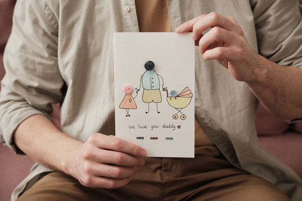 A Fathers Day card with a themed drawing and button applique is held in the hands of a man