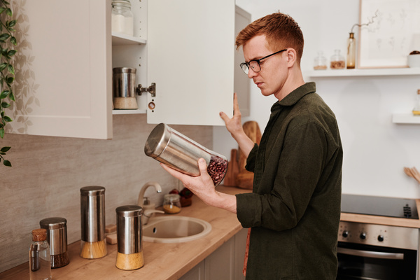 A man with red hair wearing glasses and a green shirt holding a reusable container for bulk products filled with red beans