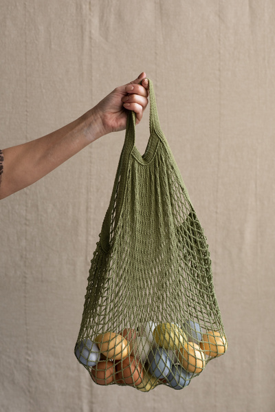 A green cotton string bag filled with Easter multicolored chicken eggs in a female hand on a light background