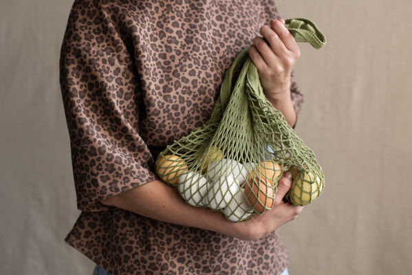 A green cotton string bag filled with Easter multicolored eggs is held in hands of a woman in a leopard print blouse