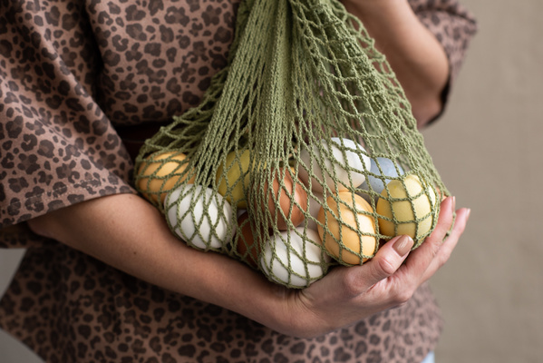 A green net bag of colorful Easter eggs in hands of a woman in leopard print clothes