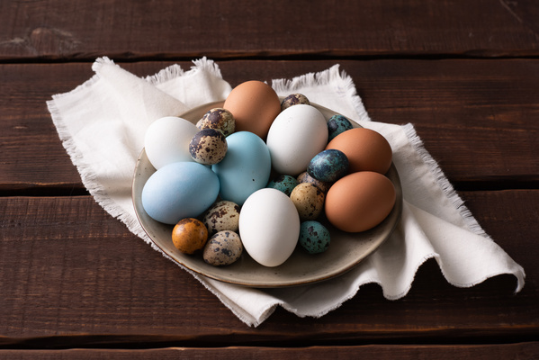 Easter chicken and quail eggs of different colors on a light plate on a white cloth napkin