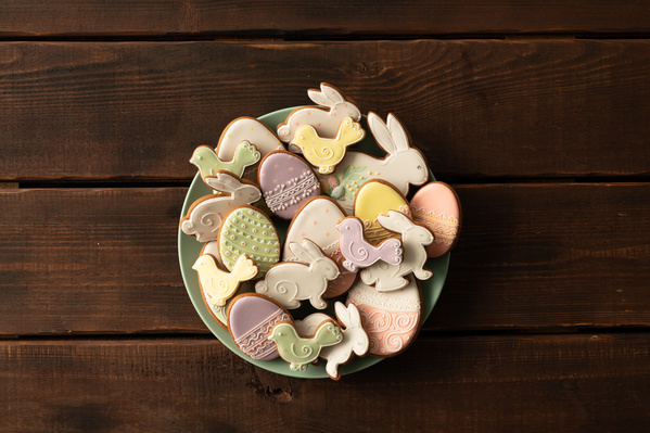 Easter glazed gingerbread cakes of different shapes on a light plate standing on a dark wood table