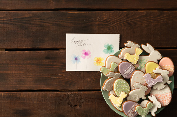 Top view of the Easter card and glazed gingerbread of different shapes in a themed style on a green plate