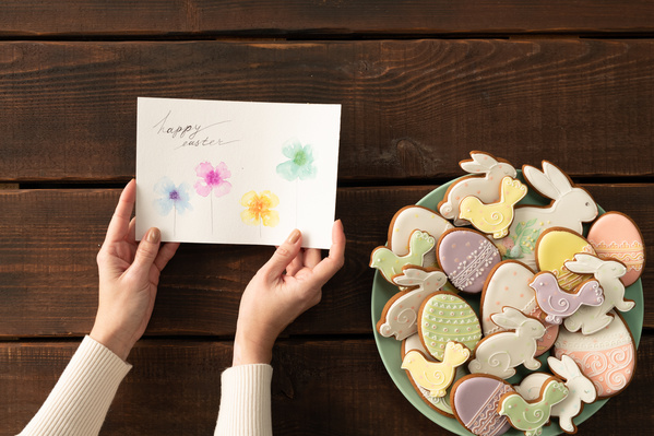 Top view of an Easter card in the hands and glazed gingerbread of different shapes in a themed style on a green plate