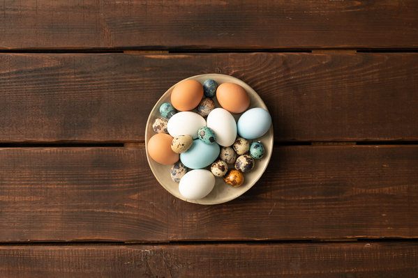 Top view of a beige plate filled with Easter quail and chicken eggs and standing on a dark wooden surface
