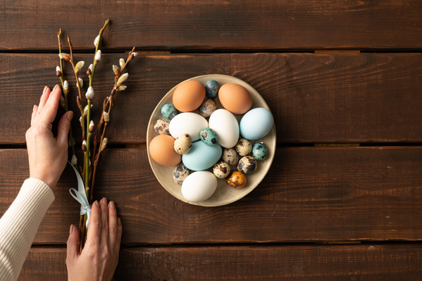 A beige plate of Easter quail and chicken eggs and a bouquet of willow twigs touched with female hands