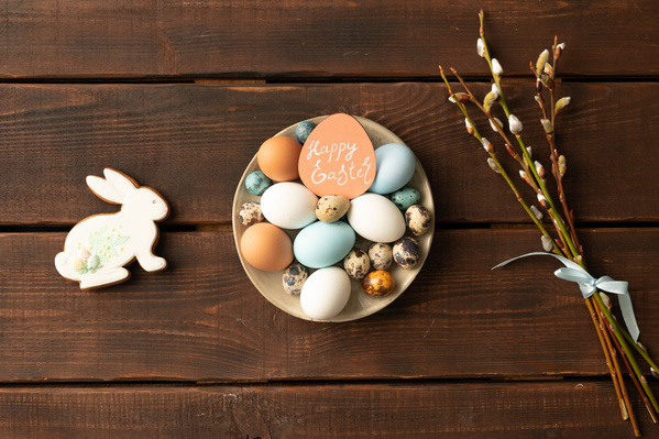 Beige plate with Easter quail and chicken eggs a bouquet of willow twigs and a festive gingerbread