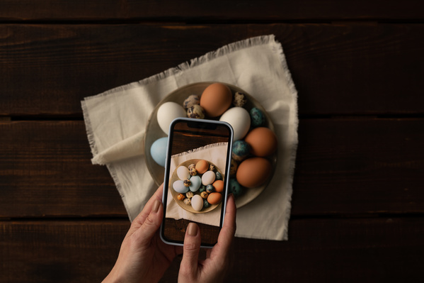 Taking a photo on a smartphone of a light dish with Easter chicken and quail eggs on a white cloth napkin with fringe on the edges.