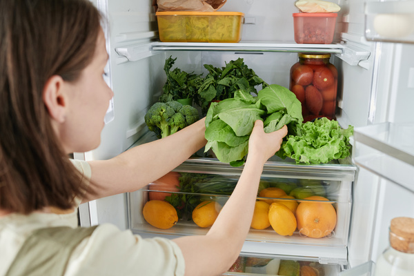 A woman with short dark hair putting fresh greens in a refrigerator filled with nutritious foods
