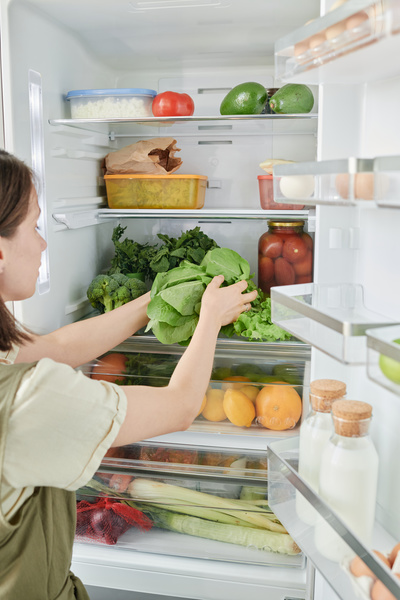 A woman with short dark hair putting fresh greenery in a refrigerator filled with healthy foods