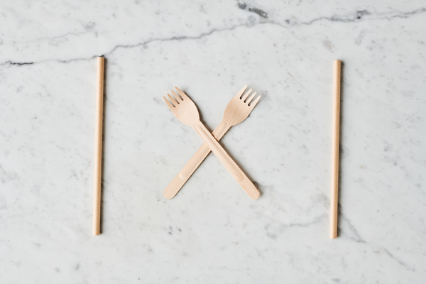 Crossed disposable organic forks with straws for drinks on a marble surface