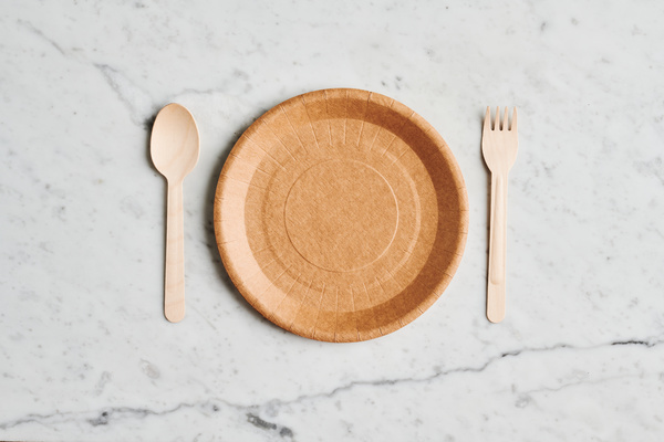 A served disposable paper plate with eco-friendly cutlery on a marble surface