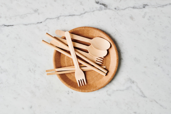 Disposable eco-friendly cutlery laid out in a brown paper plate on a marble surface