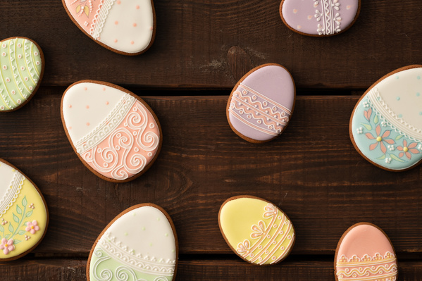 Top view of colorful glazed Easter gingerbread in the form of eggs with a thematic pattern on the surface of dark wood