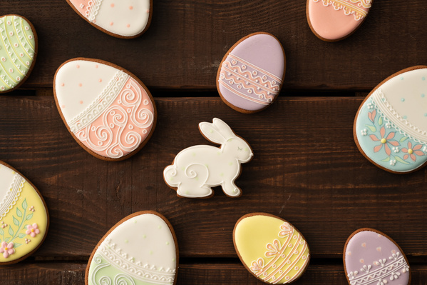 Top view of glazed Easter gingerbread of various shapes with a thematic pattern scattered on a dark wood surface