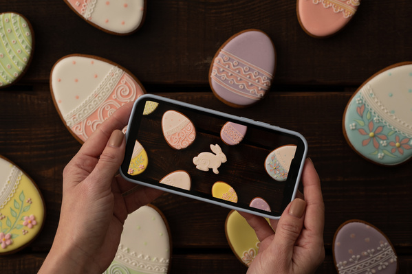Taking photo on a smartphone of Easter gingerbread in colorful icing scattered on a dark wood table