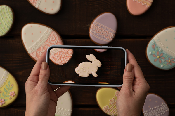 Photographing with a smartphone of Easter treats in colorful glaze spread on a dark wood table
