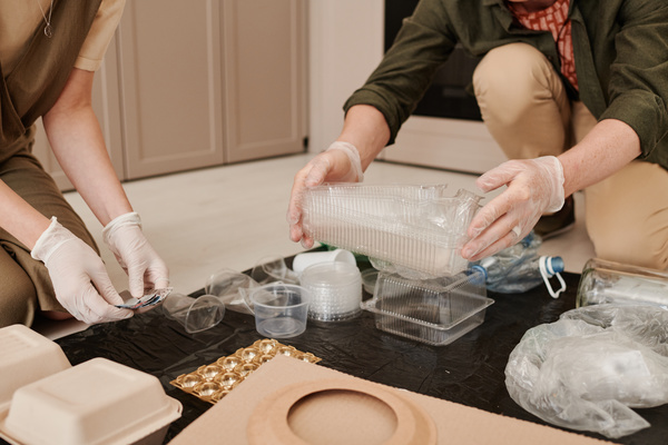 Plastic trash is prepared by a man and a woman in rubber gloves for separate collection sitting on the floor