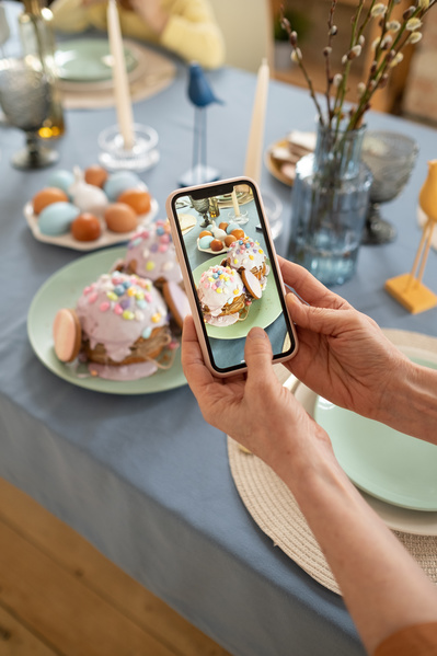 Taking a photo on a smartphone of a green plate with Easter cakes in glaze and eggs on a festive Easter table with a blue tablecloth