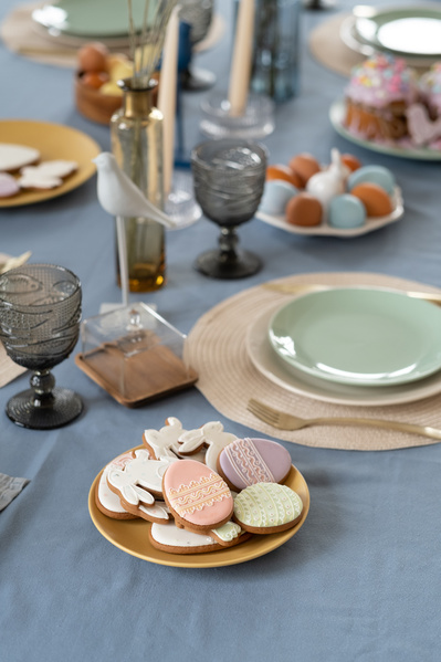 A festive setting of Easter table in light tones with a plate full of glazed gingerbread in a themed style