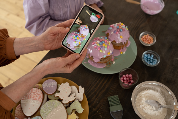 Taking photo on the phone of Easter cakes in pink glaze that the girl decorates with colorful candies