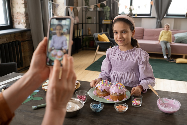 Taking a photo on the phone of a girl in a pink blouse with Easter cakes in pink glaze that she decorated with colored candies