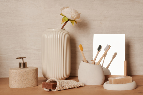 Eco toothbrushes in a toothbrush holder and natural solid and liquid soap on a wooden table with a flower in a beige vase