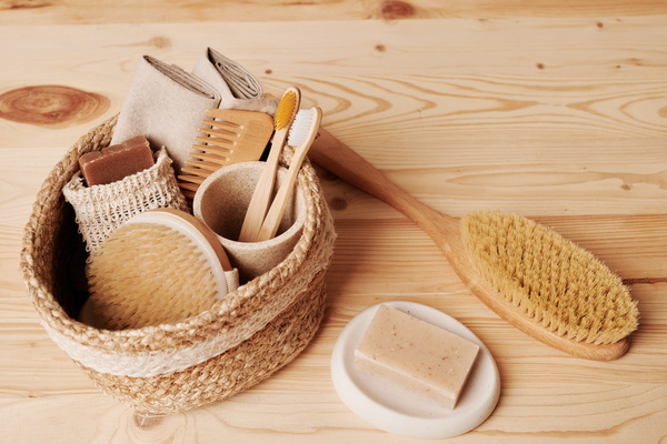 Eco-friendly toiletries in a round wicker basket on a wooden table with bar of natural soap in a soap dish and a brush for dry massage