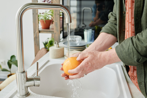 Grapefruit is washed under a stream of water in a white kitchen sink