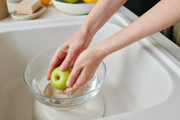 A green apple is washed in a glass bowl being in a white sink