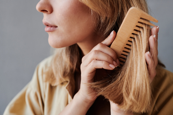 Close-up of blonde hair that is being tidied up by a woman with a wooden comb