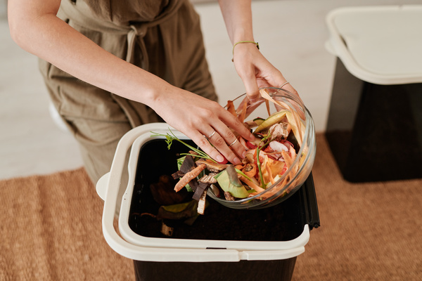A woman with short dark hair adding natural waste to the soil in a black bucket sitting on the kitchen floor