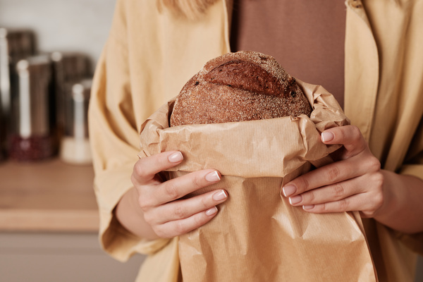 Rye bread in a paper bag in the hands of a woman dressed in light clothes