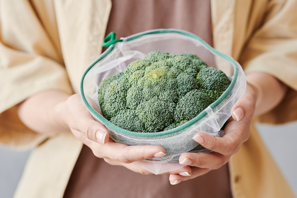 Fresh broccoli in a reusable vegetable bag with a green string in female hands