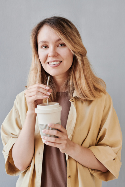 A woman with blonde hair dressed in beige clothes with a reusable white cup with an iron straw