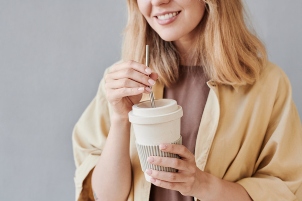 A smiling woman holding an environmentally friendly white cup for hot drinks with an iron straw