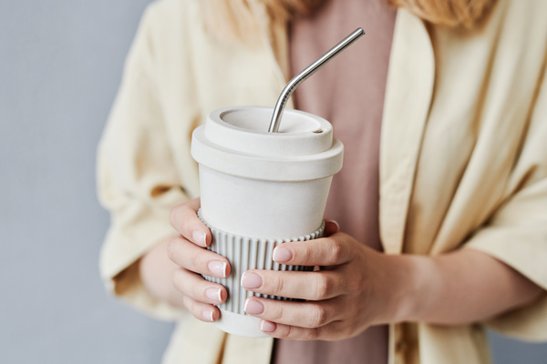 Close-up of a reusable white cup with a metallic eco-straw in female hands