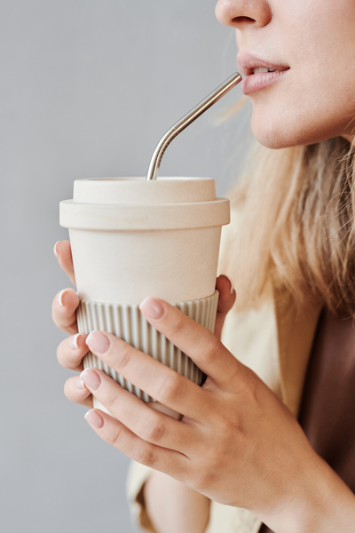 Reusable white coffee cup with metal eco-friendly straw in womens hands