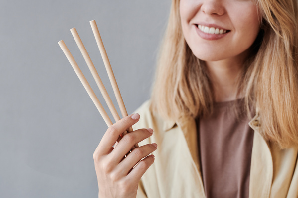 A smiling woman with blonde hair holds paper eco straws in her hand