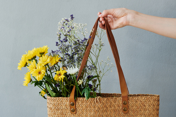 A brown braided shopper filled with bright flowers in a female hand